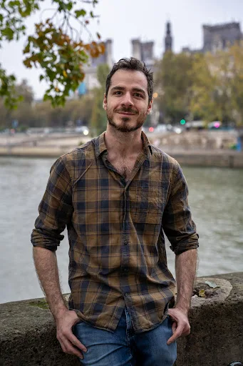 Portrait d'un homme souriant en chemise à carreaux, quais de Seine avec la cathédrale Notre-Dame en arrière-plan
