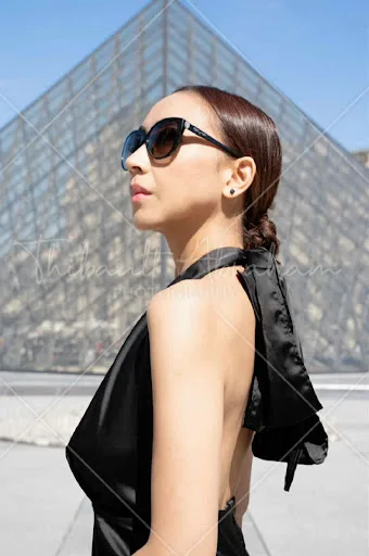 Portrait de profil d'une femme en robe noire devant la pyramide du Louvre