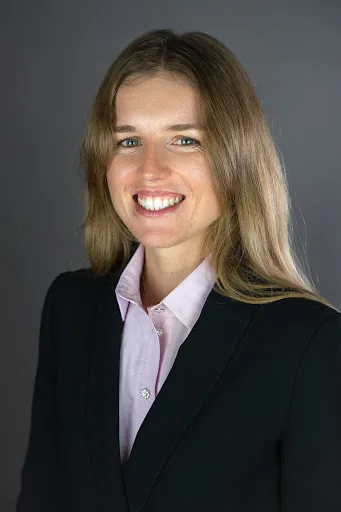 Portrait corporate en studio d'une femme en chemise rose et blazer noir, fond gris