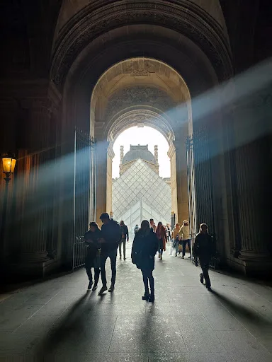Passage voûté du musée du Louvre avec vue sur la pyramide et un rayon de lumière (photo partagée sans lien avec une séance photo)